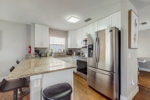 Enjoy cooking in this kitchen with a central island, bar stools, stainless steel appliances, and white cabinetry.