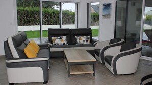 A modern living room with a grey and white sofa set, a wooden coffee table, and a glass door leading to a garden. - House with 30°C pool and enclosed garden 300m from Les Amiets beach - Bretagne (Cléder)