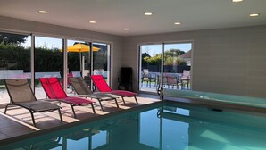 An indoor swimming pool with clear glass walls, surrounded by lounge chairs and a yellow umbrella. - House with 30°C pool and enclosed garden 300m from Les Amiets beach - Bretagne (Cléder)