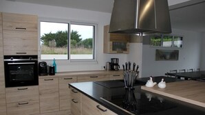 A modern kitchen with a large window, built-in oven, and stainless steel range hood. - House with 30°C pool and enclosed garden 300m from Les Amiets beach - Bretagne (Cléder)