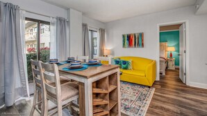 A dining area with a wooden table and chairs, a yellow sofa, and a colorful rug. - Stylish Condo CDC Standards Private Balcony 2BD 2BA 6en165 (Orlando)