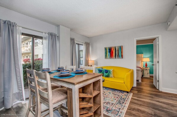 Un comedor con una mesa y sillas de madera, un sofá amarillo y una alfombra colorida.