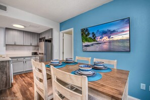 Una cocina moderna con armarios grises, una mesa de comedor de madera dispuesta con cuencos azules y blancos, y un cuadro de una playa en la pared.