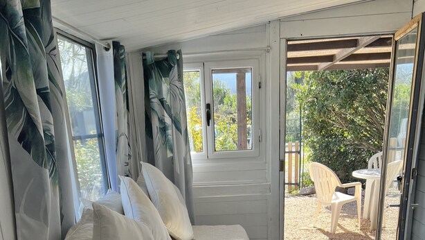 Ein Schlafzimmer mit einem Bett, weißen Vorhängen und Blick auf eine Außenpatio-Terrasse.