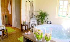 Ein Zimmer mit einer Badewanne, Holzboden, einer grünen Matte, einem kleinen Tisch mit Kerzen und einer Topfpflanze.
