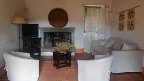 Un salon avec une cheminée, un téléviseur et deux fauteuils blancs.