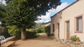 Un chemin de gravier mène à un bâtiment aux murs en pierre et aux encadrements de fenêtres roses.