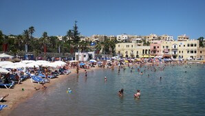 A crowded beach with people swimming and sunbathing, umbrellas, and beach chairs. - Seafront Apartment in Sliema With Pool, Upmarket Complex (Sliema)