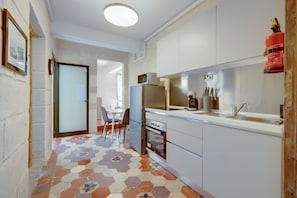 Compact kitchen with oven, microwave, and sink, featuring a geometric tile floor and a door to another room.