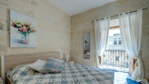 Een slaapkamer met een bed, een schilderij, een nachtkastje, een raam met gordijnen en uitzicht op een balkon.