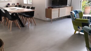 Un comedor con mesa de madera y sillas negras, un televisor sobre un mueble de madera, y un ventanal con vistas a zonas verdes.