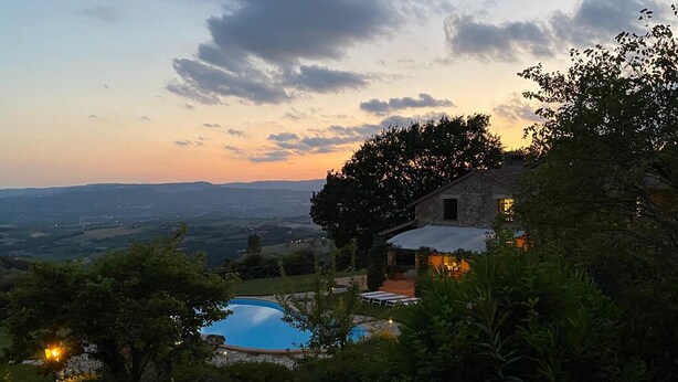 Una casa de piedra con piscina, rodeada de abundante vegetación y vistas a un valle.