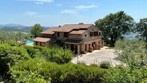 Una casa de piedra rústica con tejado de baldosas, rodeada de abundante vegetación y una vista despejada del campo.