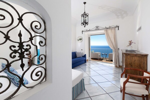 Une pièce avec un balcon, un canapé bleu, une chaise en bois et une grille en fer décorative.