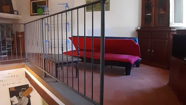 Una escalera con barandilla metálica, un sofá rojo, un armario de madera y una araña.