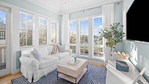 Un salón amplio con un sofá blanco, una mesa de centro y grandes ventanas con vistas al exterior.