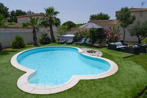 Une piscine entourée d’une pelouse parfaitement entretenue, avec des chaises longues et un jacuzzi à l’arrière-plan.