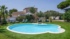 A backyard with a swimming pool, surrounded by a well-maintained lawn, palm trees, and a house with a tiled roof. - Magnificent property - 1000m² - Private Pool (Agde)