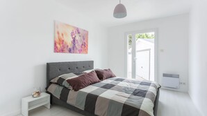 A modern bedroom with a large bed, a bedside table, a wall-mounted air conditioner, and a window with a view of greenery. - Magnificent property - 1000m² - Private Pool (Agde)