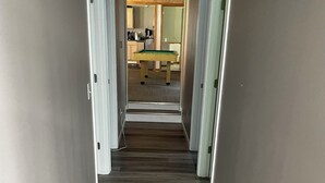 Un corridoio con pavimento in legno e pareti bianche, che conduce a una zona cucina con piano di lavoro verde e mobili in legno.