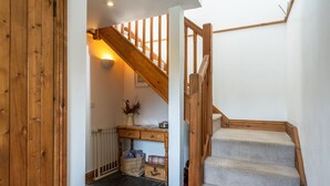 A wooden staircase with carpeted steps leading to a landing area with a desk, basket, and wall-mounted light.
