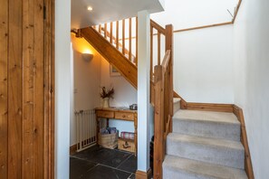 A wooden staircase with carpeted steps leading to a landing area with a desk, basket, and wall-mounted light.
