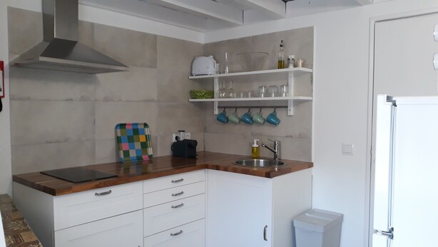 Een keuken met witte kastjes, een houten aanrecht, een roestvrijstalen spoelbak en een afzuigkap. Er staan glazen op planken en er ligt een kleurrijk dienblad.