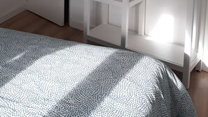 Een slaapkamer met een bed, een kledingkast met planken, een deur en een lichtschakelaar.