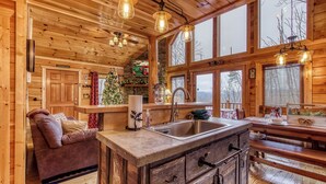 A wooden cabin interior with a kitchenette, a dining area, and a cozy seating area.