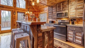 A wooden cabin interior with a kitchen, bar area, and large windows.