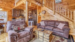 A wooden cabin interior with a sofa, a coffee table, a kitchen area, and a staircase.