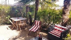 Une terrasse extérieure avec une table et des chaises en bois, une chaise de plage à rayures et un canapé en osier.