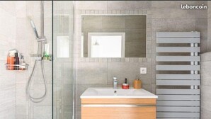 Une salle de bain moderne dotée d’une douche à parois de verre, d’un meuble-lavabo en bois avec un vasque blanche et d’un porte-serviettes intégré.
