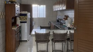A modern kitchen with a dining area, featuring a refrigerator, cabinets, and a coffee maker. - Casa de Praia Condomínio Fechado em Ipioca (Maceió)