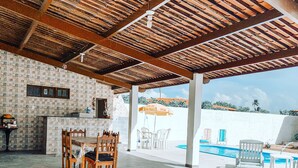 An outdoor patio with a pool, covered seating area, and a dining table with chairs. - Casa de Praia Condomínio Fechado em Ipioca (Maceió)
