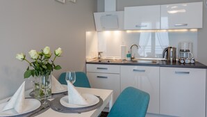 Una cocina moderna con armarios blancos, un lavamanos de acero inoxidable y una cafetera. Hay una mesa de comedor con un jarrón de rosas blancas y una copa de vino.