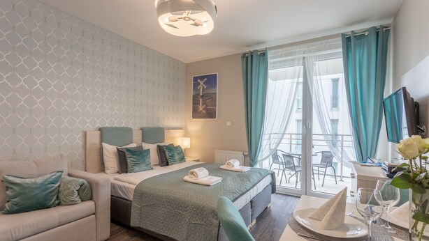 Habitación de hotel moderna con cama, sofá, mesa de comedor con platos y vasos, y vista al exterior.
