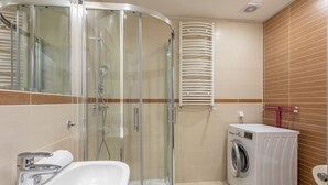 Un baño moderno con ducha envuelta en vidrio, lavadora integrada y lavamanos con espejo.