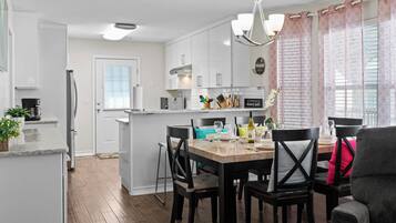 A modern kitchen with white cabinets, a central island, and a dining area with black chairs and a table.