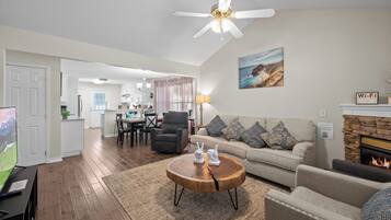 A living room with a fireplace, a ceiling fan, and a dining area in the background.