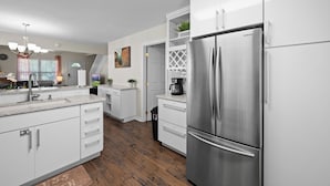 A modern kitchen with white cabinetry, stainless steel appliances, and a wooden floor. - CUTE COTTAGE, 2 Minutes to PF STRIP!! EV Charger, LOCATION! Safe and Quiet (Pigeon Forge)