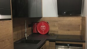 A modern kitchen with a black countertop, wooden cabinets, a stainless steel dishwasher, and a red Bistrot Cafe sign. - Chalet-style apartment, mountain view, sleeps 1 to 6 - Mont-Dore (Le Mont Dore)