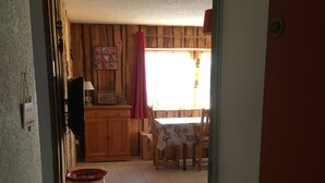 A room with a tiled floor, a wooden cabinet, a television, and a window with curtains. - Chalet-style apartment, mountain view, sleeps 1 to 6 - Mont-Dore (Le Mont Dore)
