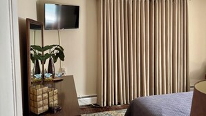 A hotel room with a bed, a television mounted on the wall, a mirror, a plant, and a curtain. - Fun Downtown Location 2nd flr (Southington)