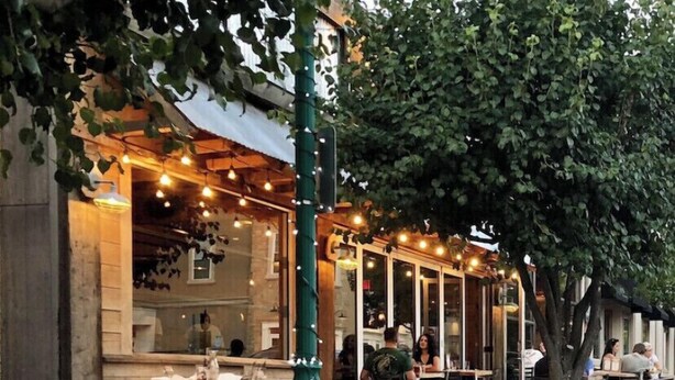 An outdoor dining area with tables and chairs, a green street lamp, and a building with large windows and string lights. - Fun Downtown Location 2nd flr (Southington)