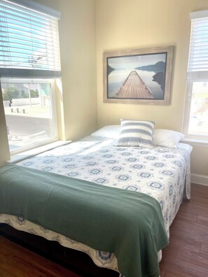 A bedroom with a bed, a painting, and a window.