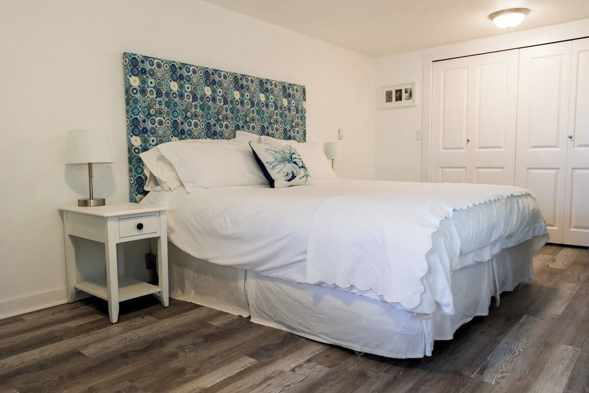 A bedroom with a bed, a nightstand, a wall art piece, and a door.
