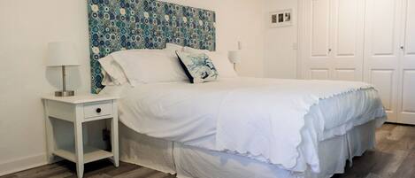 A bedroom with a bed, a nightstand, a wall art piece, and a door.