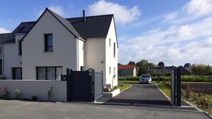Une maison moderne à deux étages, dotée d’une allée privée fermée par un portail et d’une voiture garée à l’intérieur.