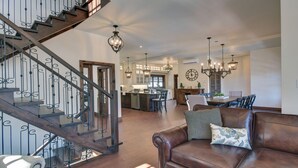 A spacious living area with a brown leather sofa, a wooden staircase with black railings, and a kitchen in the background.